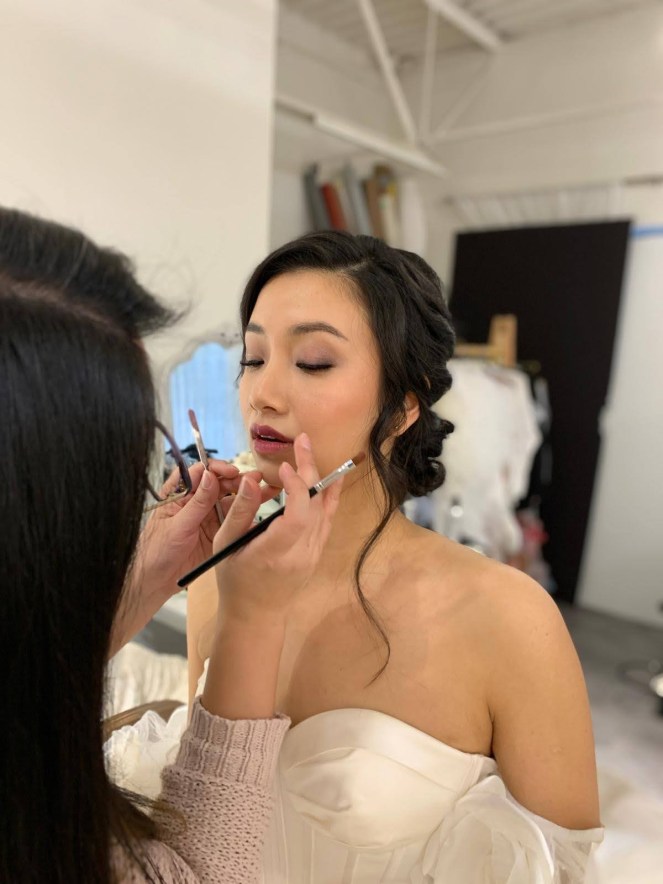 Makeup artist applying finishing touches on bride.
